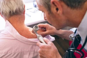 a dermatologist inspecting a man's back shoulder for a breakout